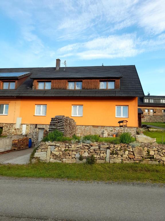an orange house with a stone wall in front of it at Apartmán u Zdeňků in Modrava