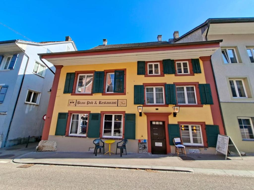 a yellow and green building with chairs in front of it at Braui Pub and Restaurant in Waldenburg