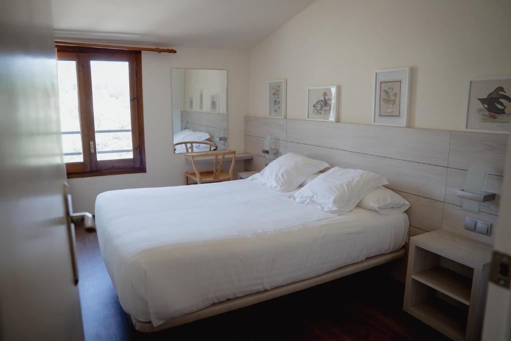 a bedroom with a bed with white sheets and a window at Hostal Bertran in Salás de Pallás