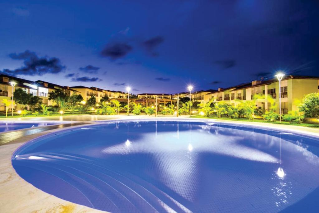 una gran piscina por la noche con edificios en el fondo en Reserva Imbassai Apartment, en Imbassai