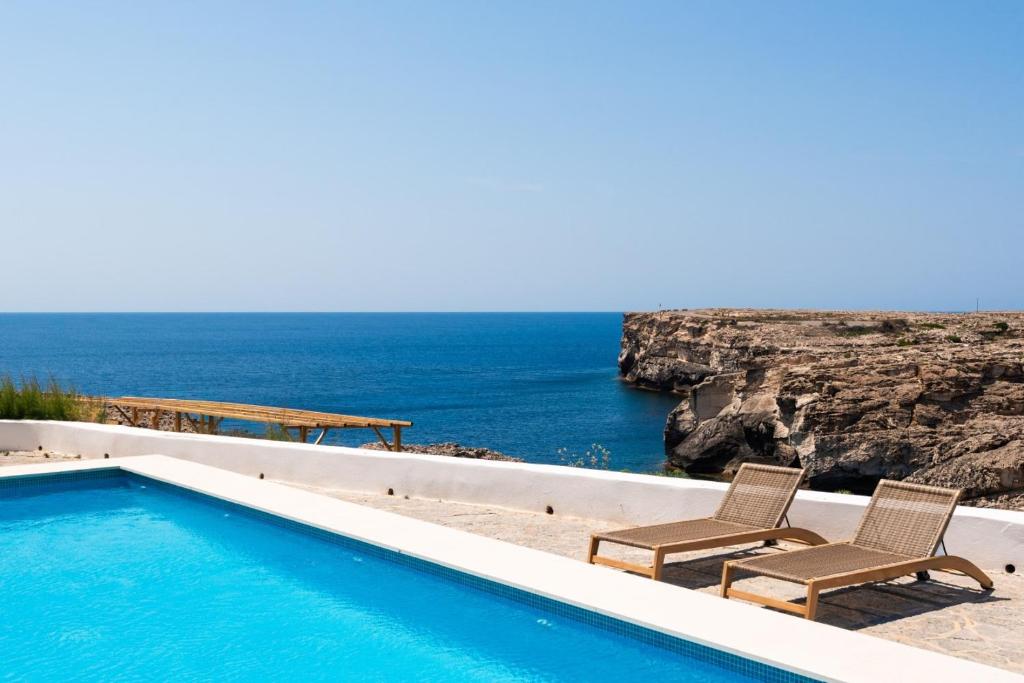 a swimming pool with two chairs and the ocean at VORAMAR by 3VILLAS in Cala en Forcat