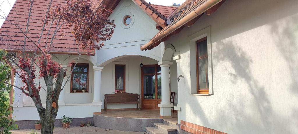 a white house with a porch and a tree at Felföldi Tanyavendégház in Kiskunmajsa