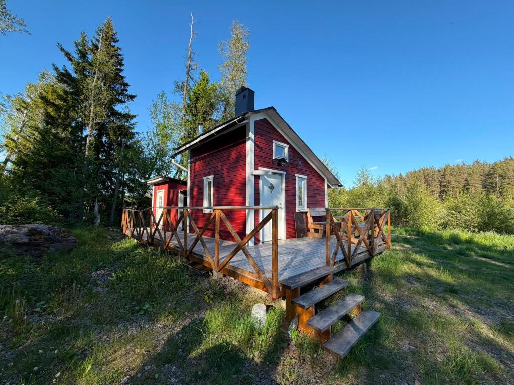 a small red house with a wooden deck in a field at The Hermits Hut in Österby