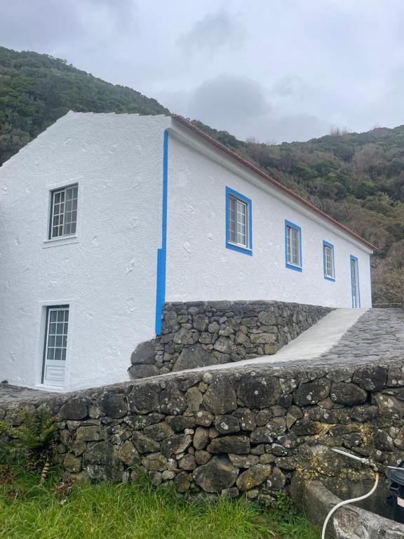 a white building with blue windows and a stone wall at Robalinho's House in Faja Grande