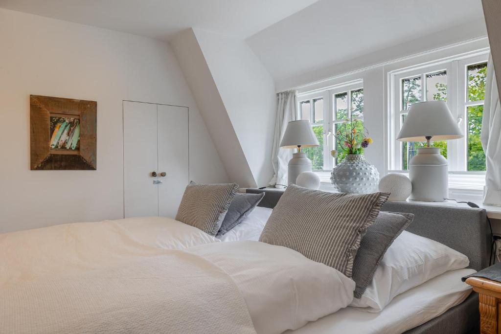 a white bedroom with a bed and two windows at Beachday Kampen in Kampen