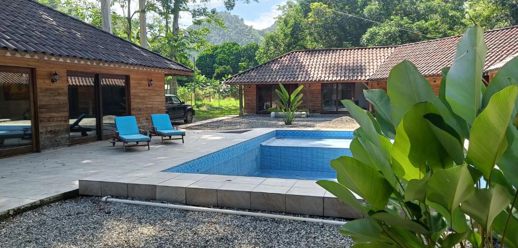 a swimming pool with two blue chairs and a house at El Sueño Belga in Golfito