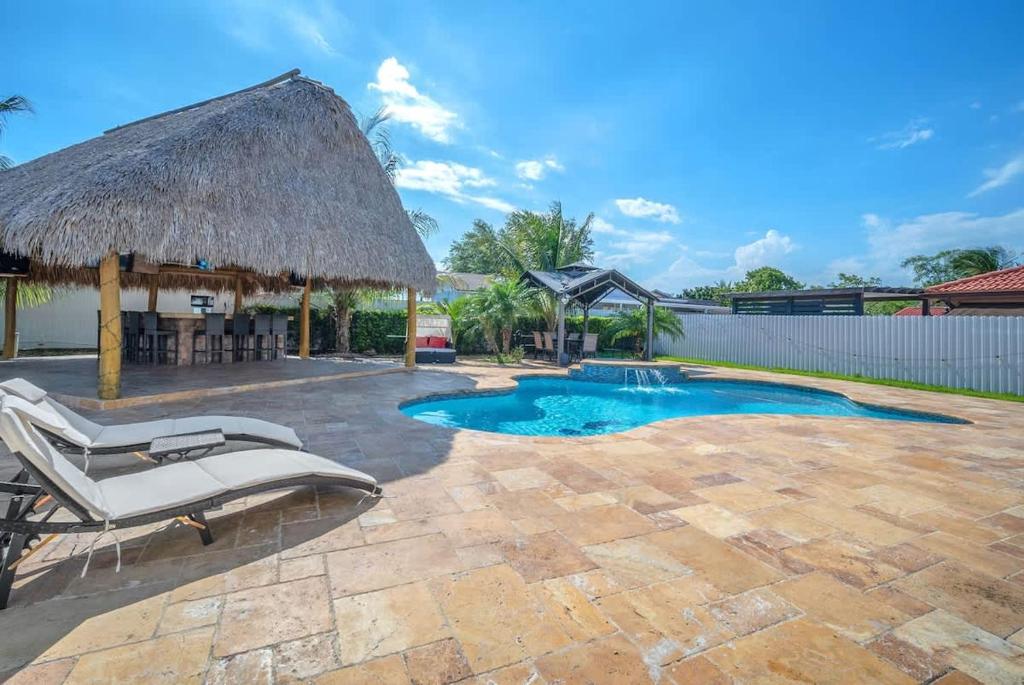 a swimming pool with chairs and a thatch roof at 6BR Villa Tropical Haven Private Pool & BBQ in Homestead