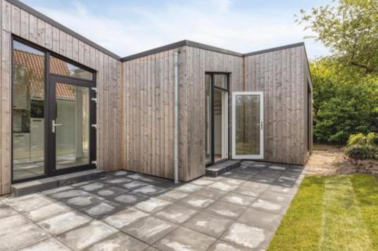a wooden house with glass doors on a patio at Sea & Forest Lodge in Oostkapelle