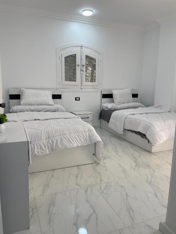 two beds in a white room with marble floors at Chez Cat & Lolo in Quseir