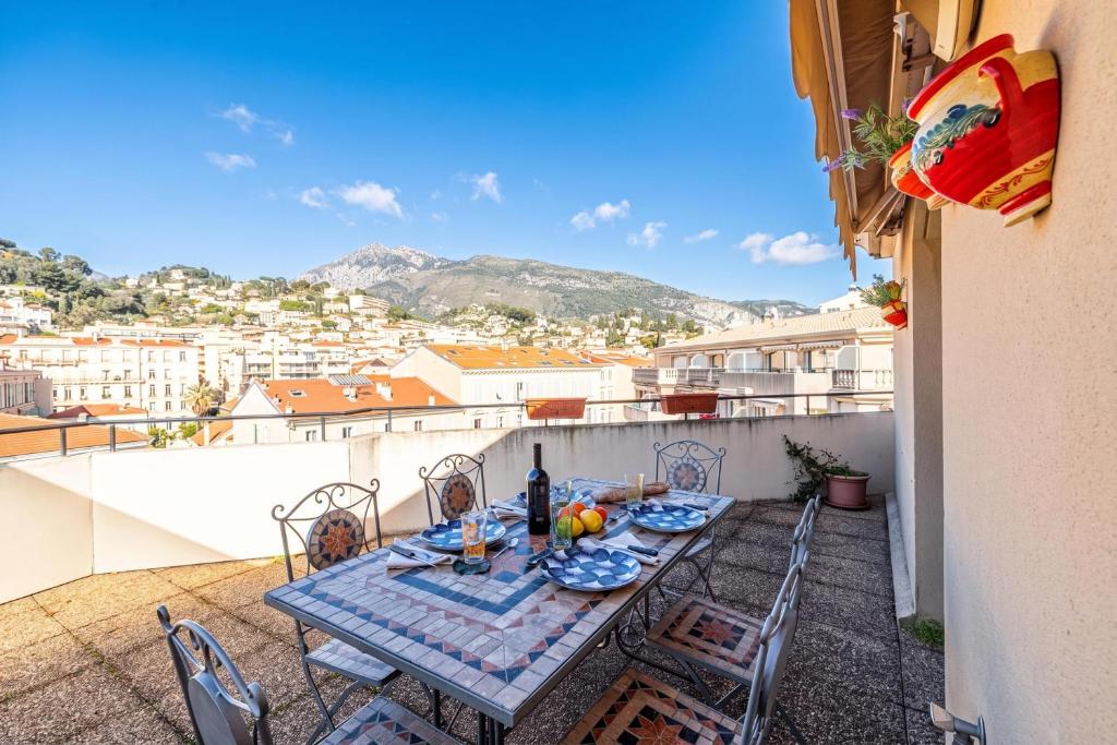 a table on a balcony with a view of a city at Victoria Bergamote Attic with Terrace and Sea View - Happy Rentals in Menton