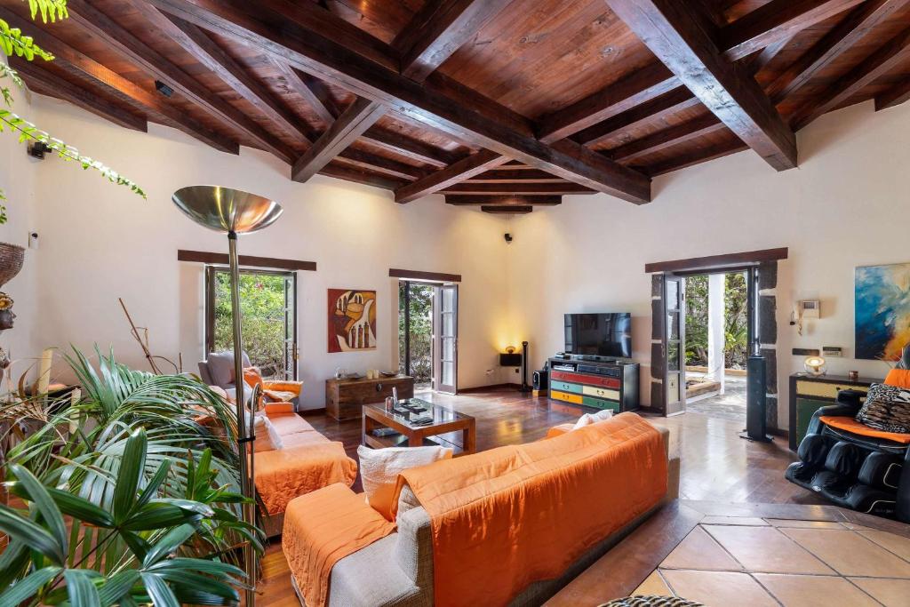 una sala de estar diáfana con muebles naranjas y techos de madera. en Villa Muller by Bayside - The Fountain of Silence, en Tías