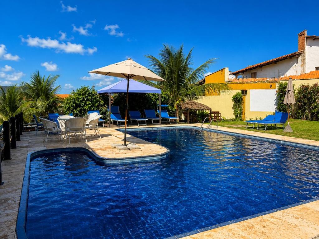 a swimming pool with chairs and an umbrella at Pousada Vila Italia - Porto da Dunas in Aquiraz