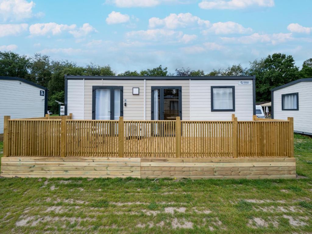 a tiny house with a wooden fence in a yard at Comfortable caravan in a green setting in Vierhuizen