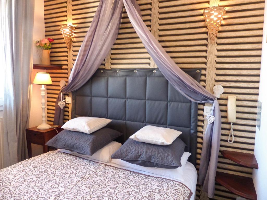 a bedroom with a bed with a canopy and pillows at Hôtel Les Embruns Sables d'Olonne in Les Sables-d'Olonne