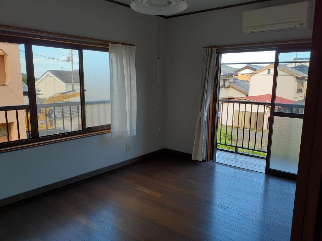 an empty room with two large windows and wooden floors at 民宿なかやま in Kushimoto