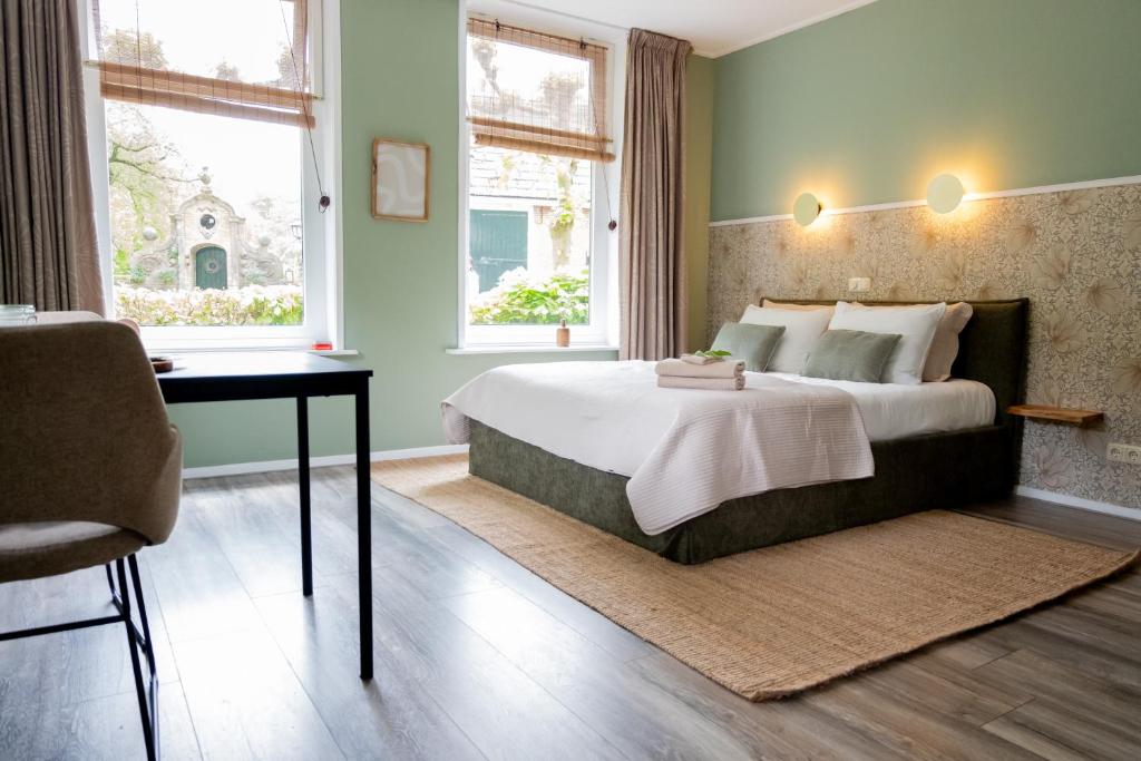 a bedroom with a bed and a desk and windows at B&B Stinzenflora - Gezellige accommodatie tussen groen en historie in Cornjum
