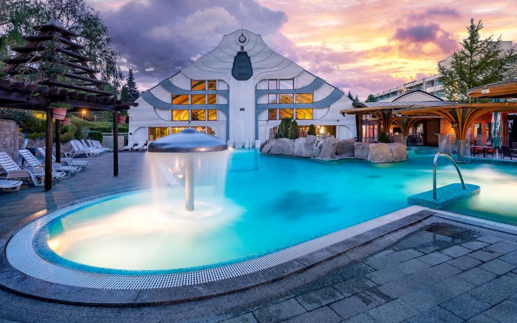 a large pool with a fountain in front of a building at Hotel Carbona Thermal Spa in Hévíz