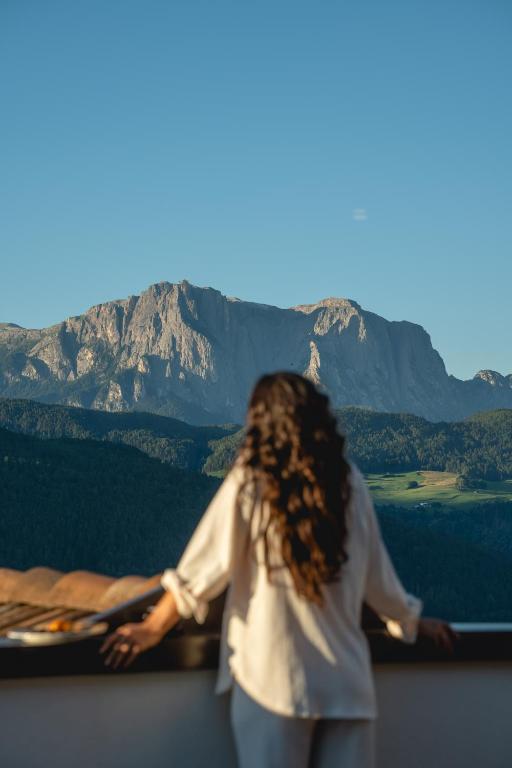 a woman standing on a balcony looking at a mountain at Granpanorama Hotel StephansHof in Villandro