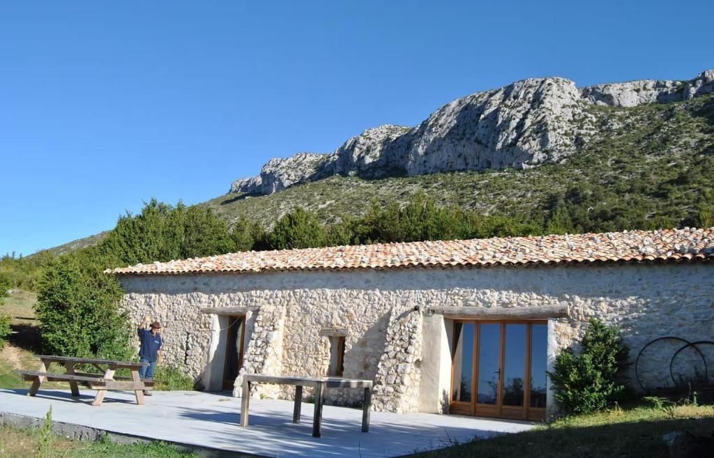a person standing next to a stone building with a mountain at Gîte bergerie in Bargème