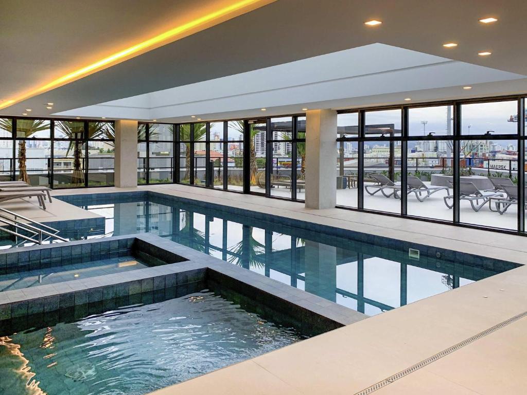 an indoor swimming pool in a building with windows at Mercure Itajai Navegantes in Itajaí