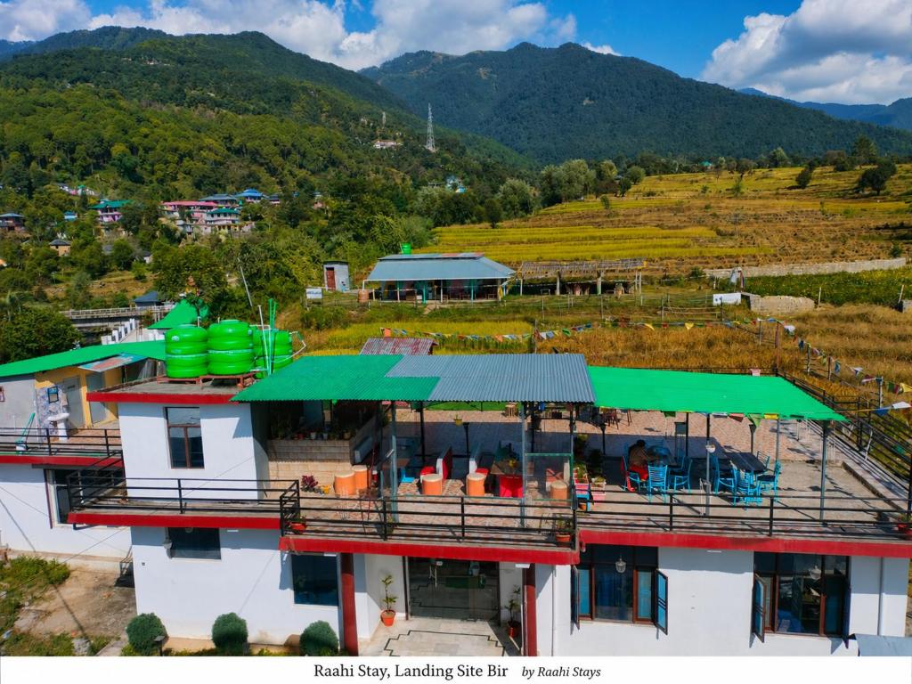 a building with a green roof with a mountain in the background at Raahi Stay, Landing site Bir - Stay & Cafe in Bīr