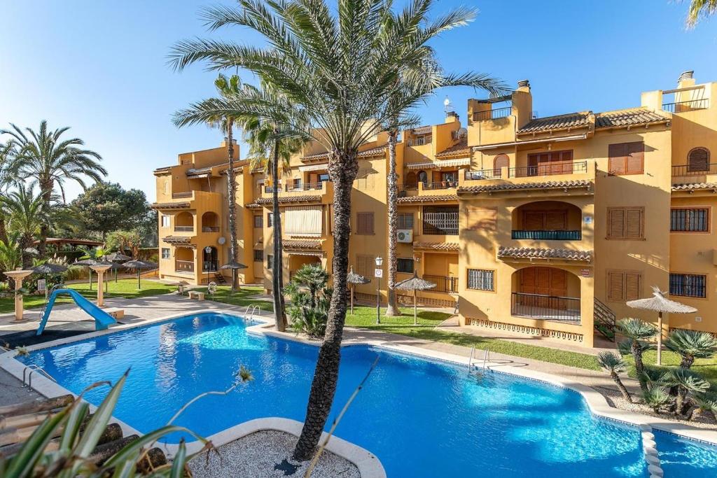 a swimming pool in front of a building with palm trees at Spacious apartment with sea view in La Mata - 75 m² - Pool in La Mata