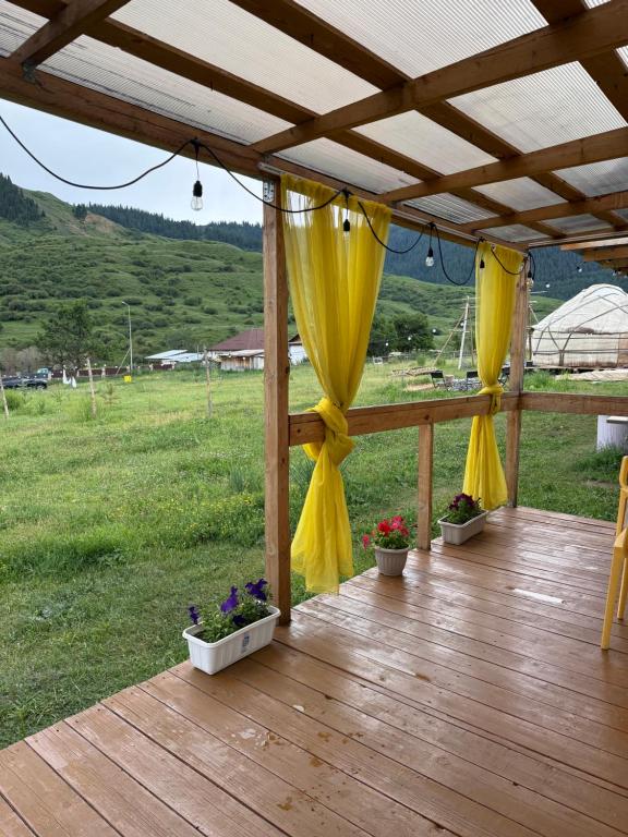 a wooden deck with yellow curtains and potted plants at Qurmety camp in Kurmenty