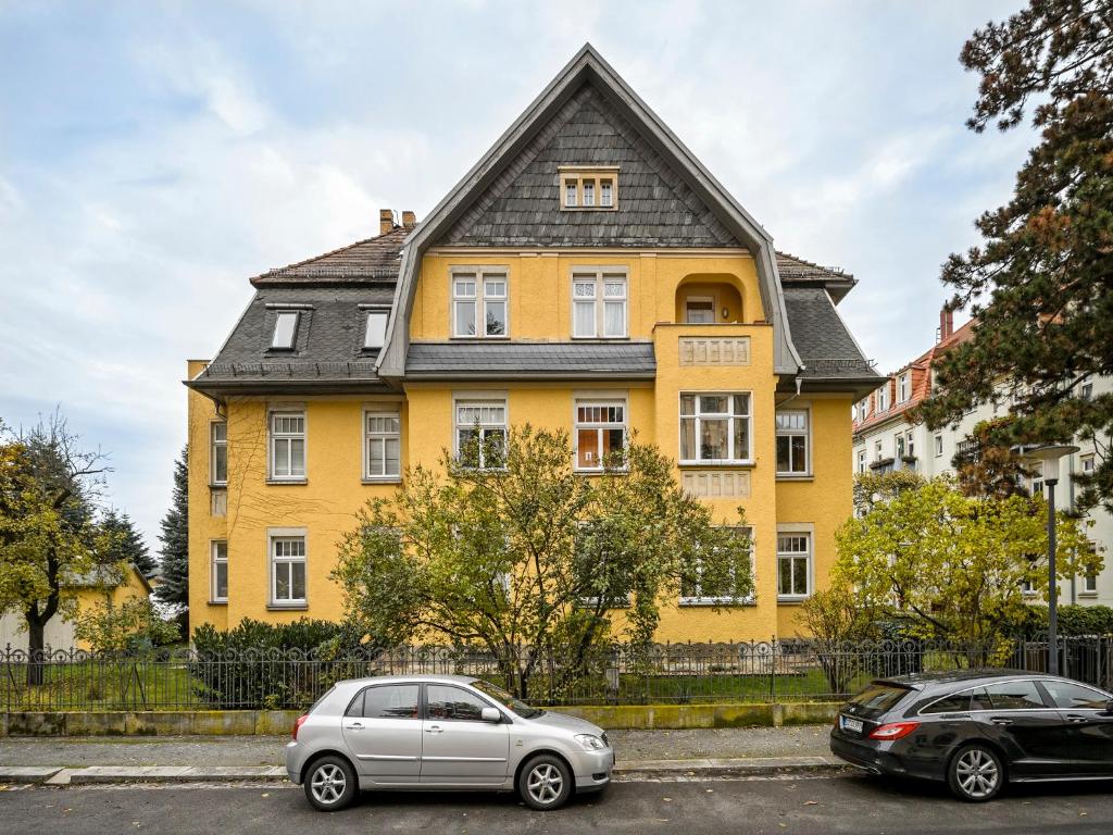 a yellow house with two cars parked in front of it at Villa Eschebach - Ferienwohnung in Dresden