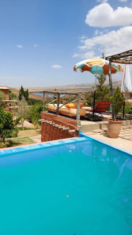 a blue swimming pool with an umbrella and a table at dar boumida in Lalla Takerkoust