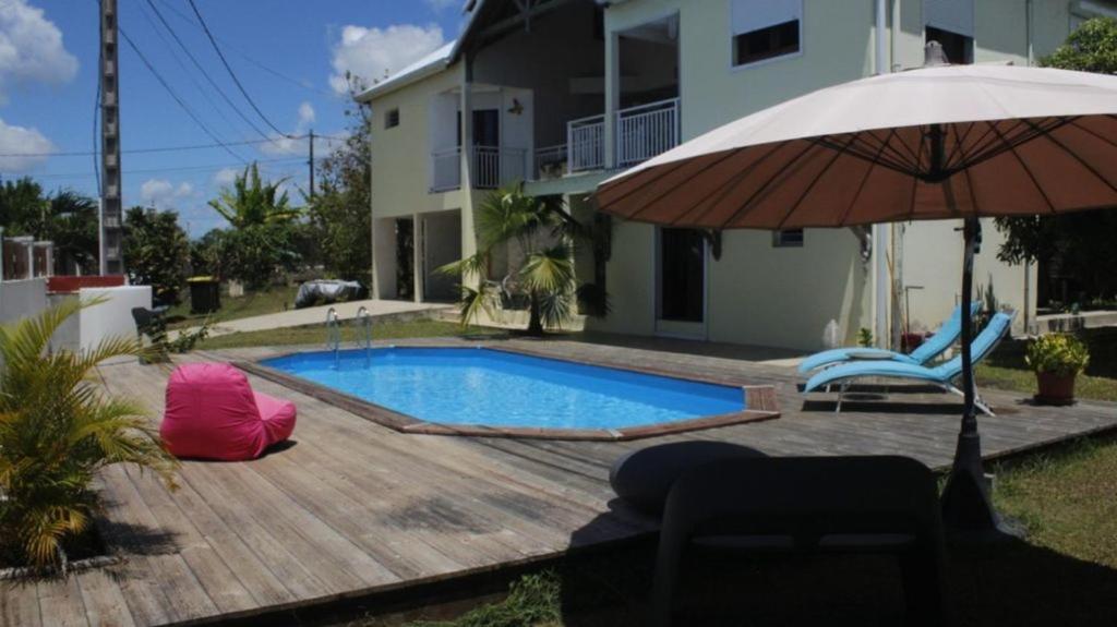 a swimming pool with an umbrella and a chair and an umbrella at Studio accueillant à Baie Mahault, 22 m², piscine partagée. in Baie-Mahault