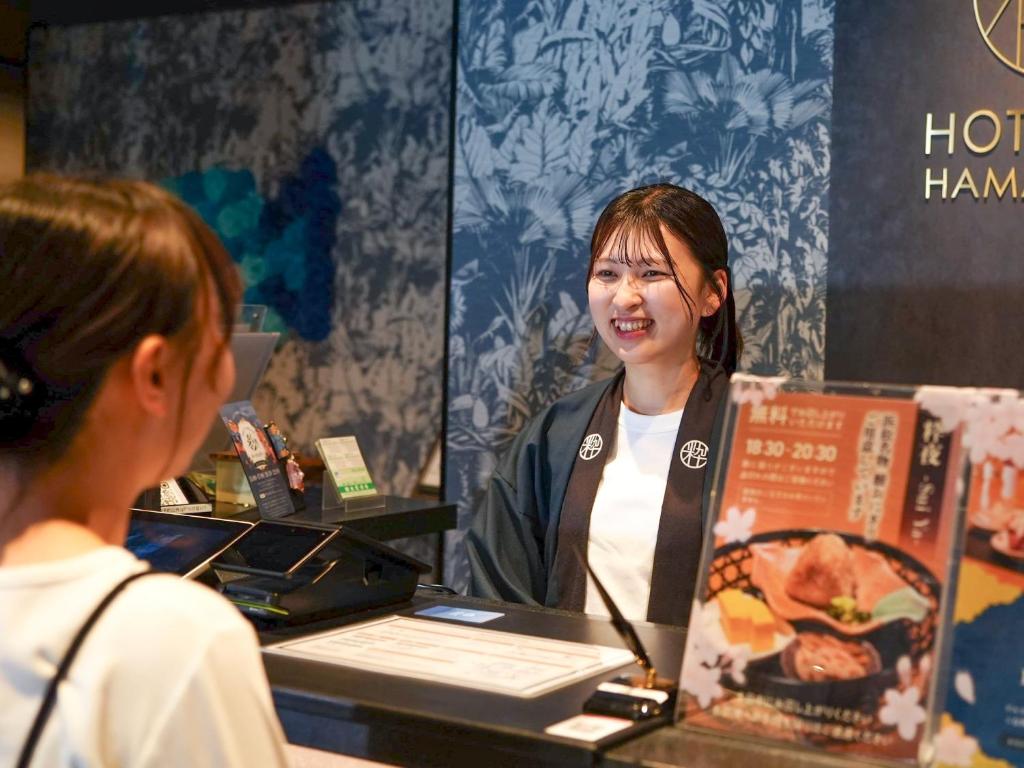 a woman standing behind a counter talking to a customer at HOTEL SUI HAMAMATSU by ABEST in Hamamatsu
