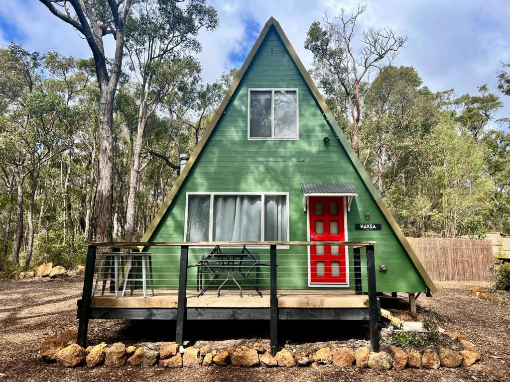 a green house with a red door in a yard at Hakea at Porongurup Chalets in Porongurup