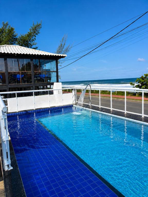 a swimming pool next to a fence and the ocean at Pousada Viva Mar in Saquarema