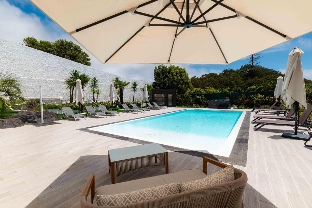 a swimming pool with chairs and an umbrella at Gaivota Guest House in Ponta Delgada
