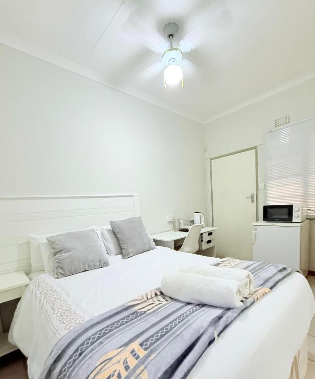 a white bedroom with a bed and a ceiling fan at Paradise Corner in Francistown