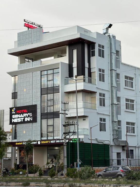 a white building with a sign in front of it at Senary's Nest INN in Kyātsandra