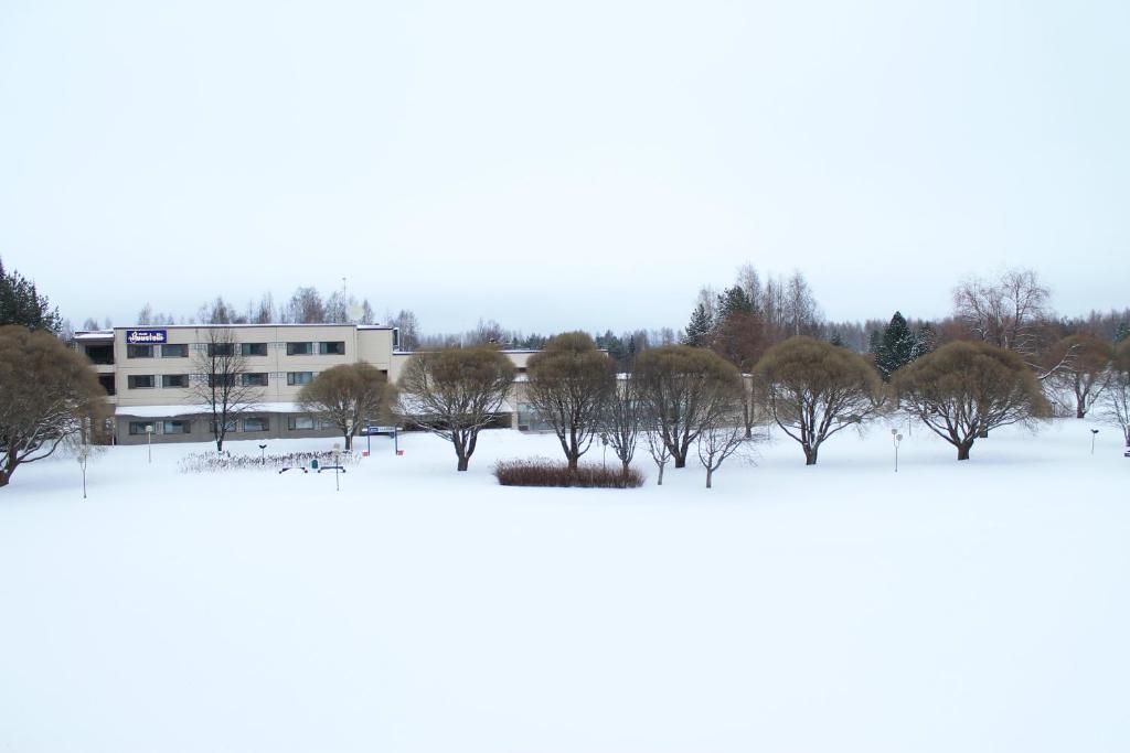 a building in the snow with trees in the foreground at Hotelli Puustelli Lieksa in Lieksa