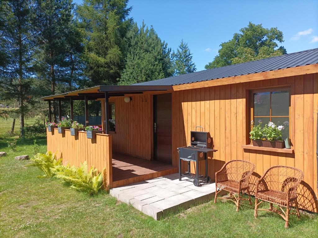 a wooden cabin with a deck with chairs and a stove at Zielona Polana in Debrznik