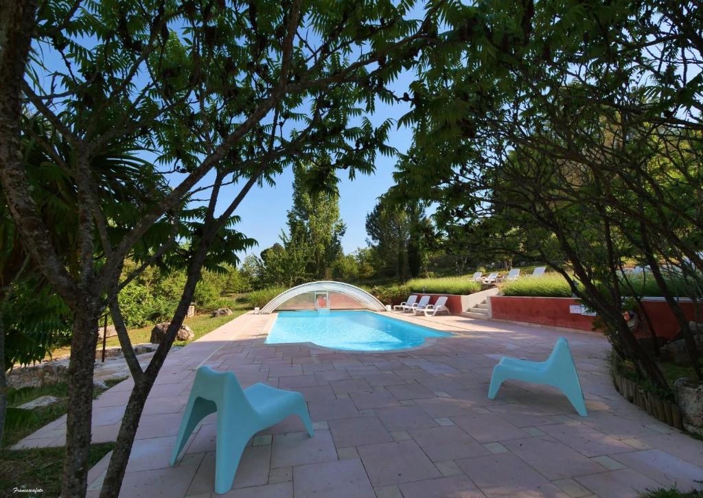 a swimming pool with two blue chairs and trees at Campagne SAINT MAURINET in Montmeyan