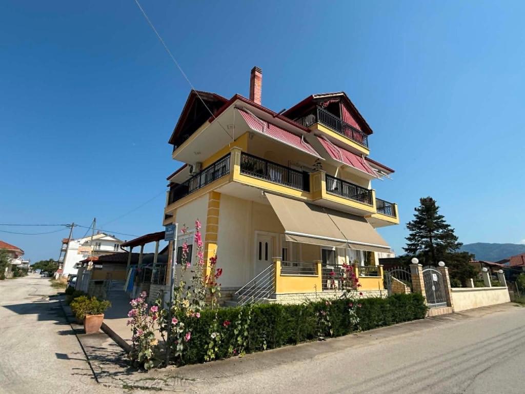 a yellow and white building with flowers in front of it at Themis Rooms in Nea Vrasna