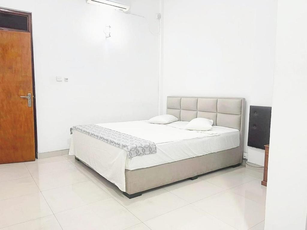 a white bedroom with a bed and a wooden door at Mount View Hotel Badulla Room 02 in Badulla