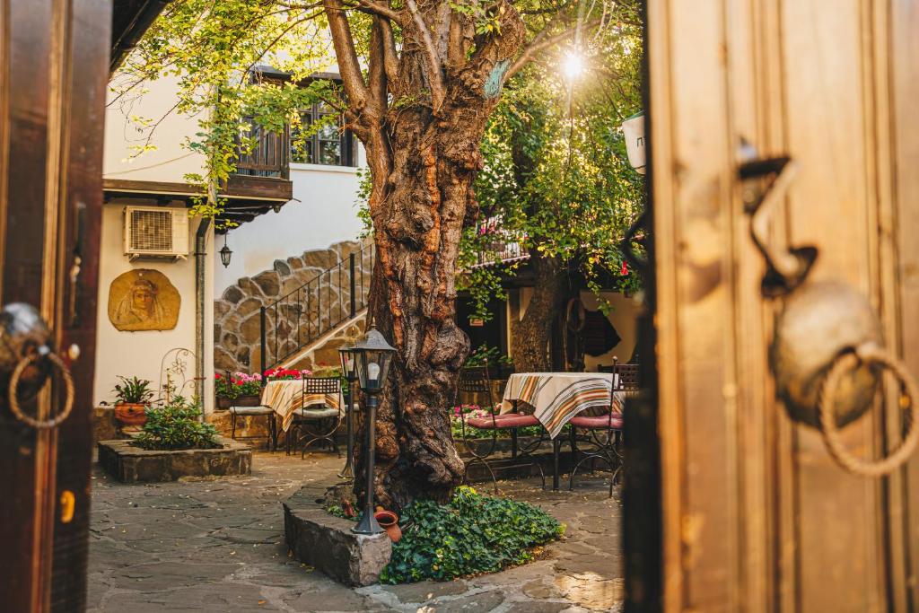 a tree in a courtyard with a table and chairs at Oazis Family Hotel in Lovech