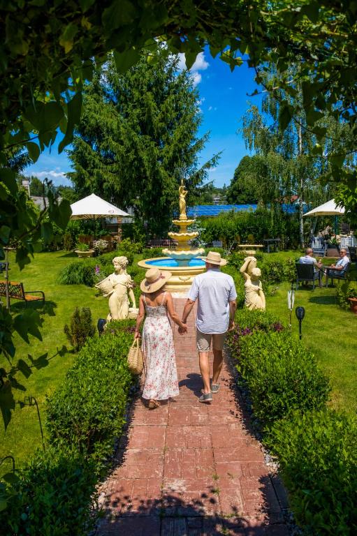 Ein Mann und eine Frau gehen einen Backsteinweg entlang zu einem Brunnen in der Unterkunft Hotel Tommy Wellness & Spa in Náchod