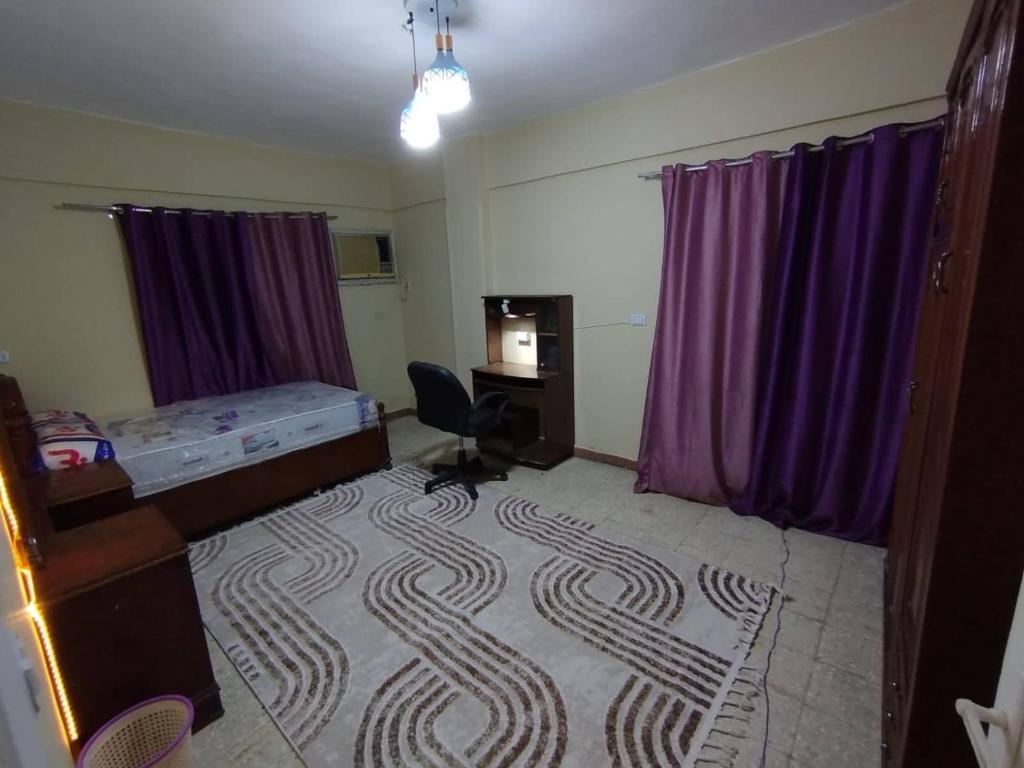 a room with a bed and a desk and purple curtains at ابراهيم هاوس in Al Ghuşnah