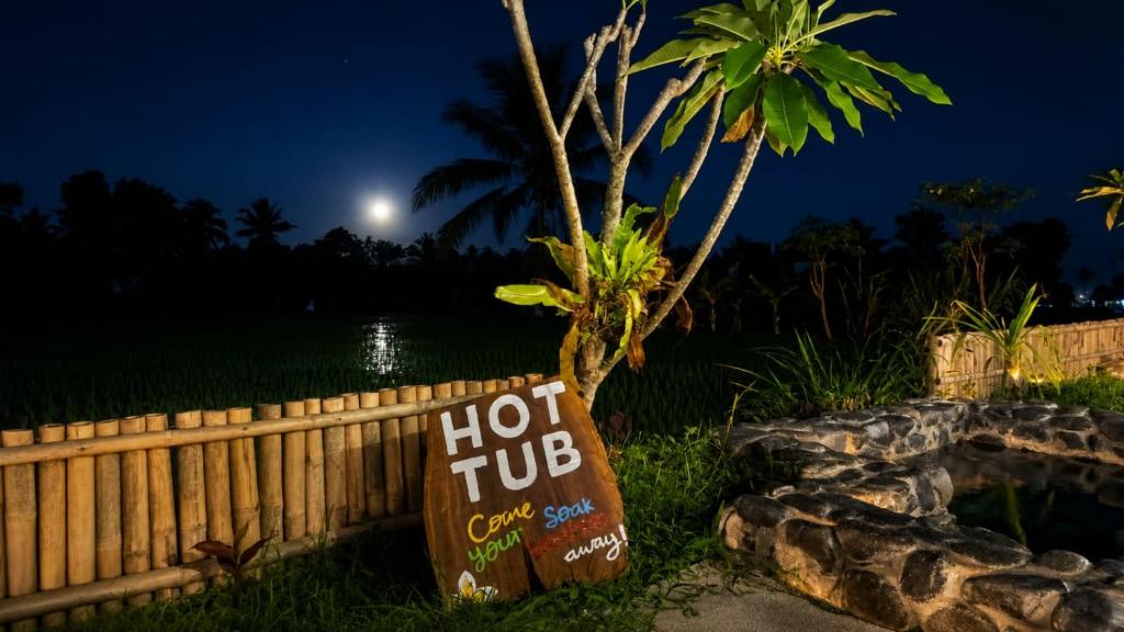 a hot tub sign in front of a palm tree at night at Nêst Guesthouse Tetebatu in Tetebatu