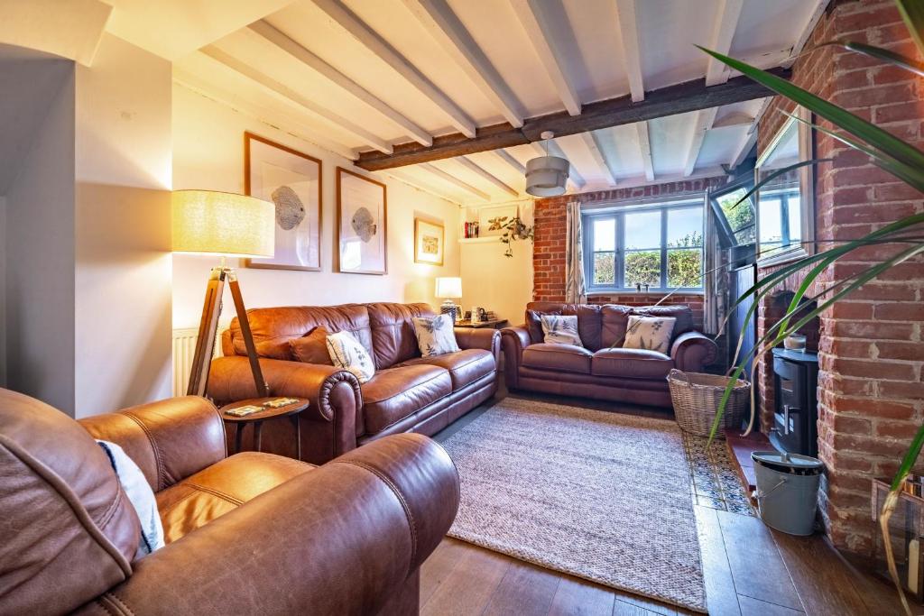 a living room with leather furniture and a brick wall at Ruthie Cottage in Bacton