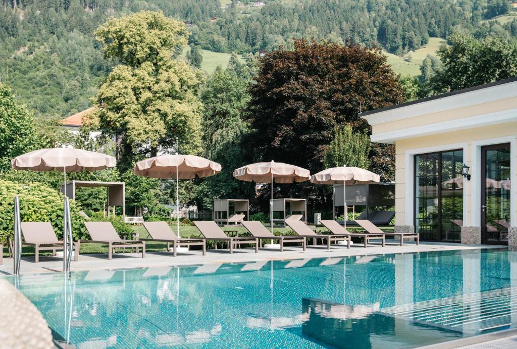 ein Pool in einem Hotel mit Liegestühlen und Sonnenschirmen in der Unterkunft Hotel Bräu in Zell am Ziller