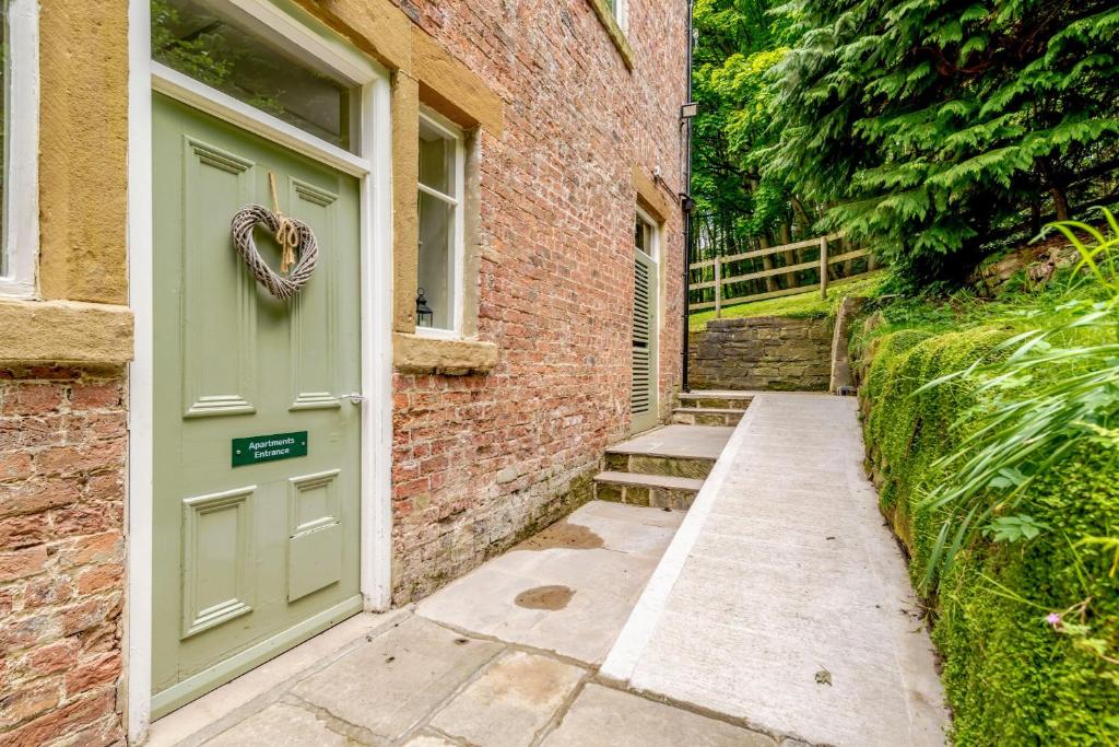 a green door with a heart wreath next to a brick building at Cote Ghyll Mill Holiday Apartments in Osmotherley