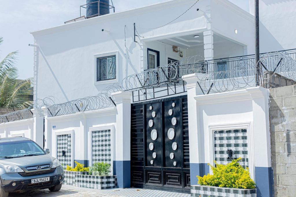 a white house with a black gate and a car parked in front at Sowe's Villa in Old Yundum