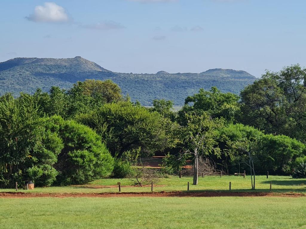a field with trees and mountains in the background at Mountain Sanctuary Park in Rustenburg